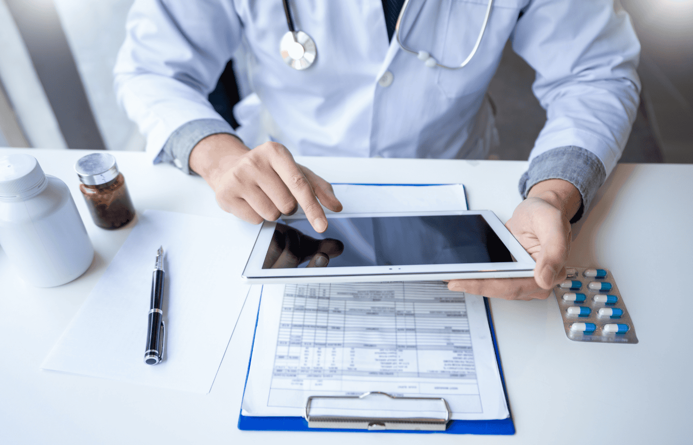 Doctor reviewing patient records on a tablet, with medication bottles and a clipboard containing patient data, illustrating manual data migration strategy in healthcare.