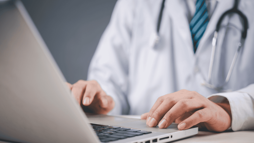 Healthcare professional typing on laptop, emphasizing data governance and electronic health record management for quality improvement initiatives.
